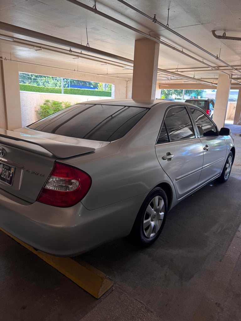 Silver sedan parked in covered parking garage with concrete pillars and overhead lighting