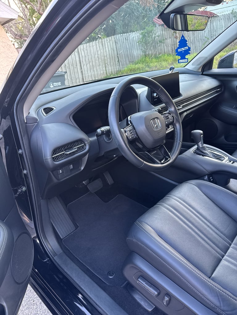 Interior view of a Honda vehicle showing the steering wheel, dashboard, center console, and gray leather seats with an open driver-side door
