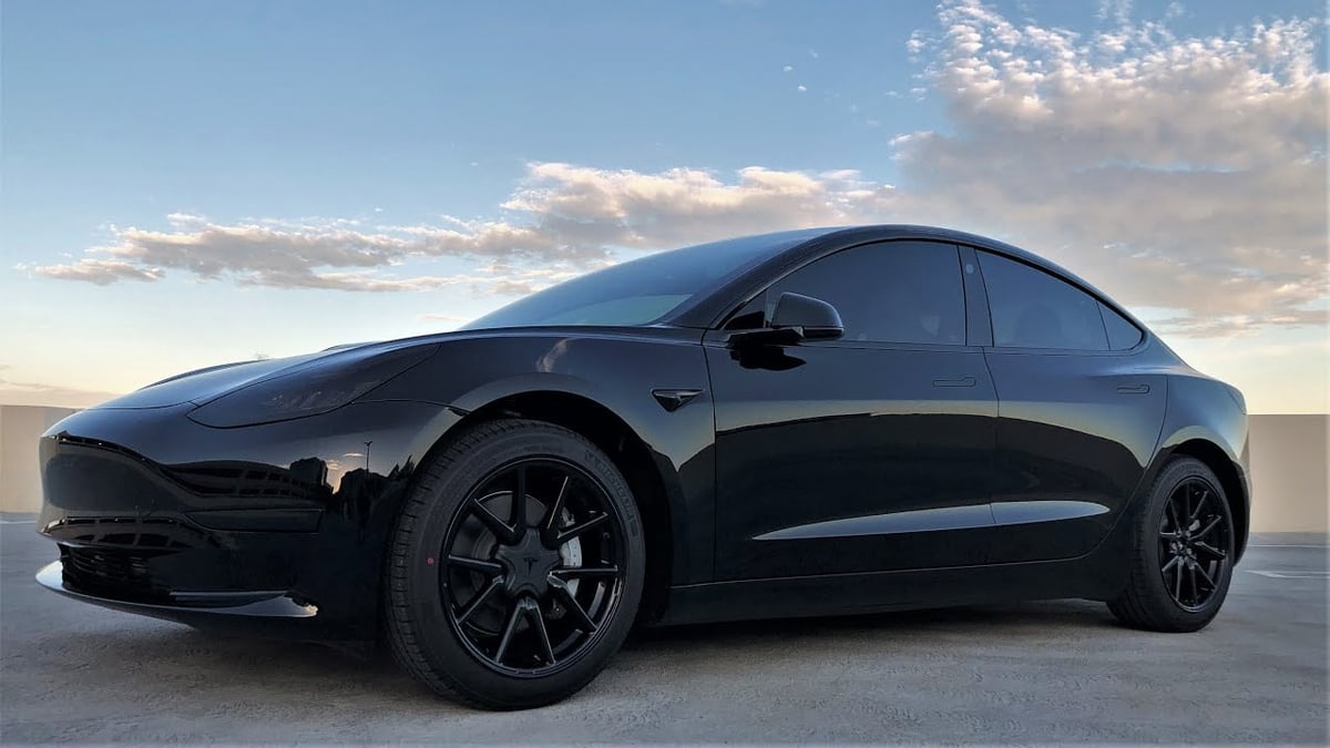 Black electric sedan parked in desert landscape with blue sky and clouds behind it